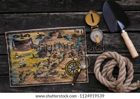 Treasure map, compass, shovel, mignifying glass and rope on old wooden table background. Treasure hunter concept.