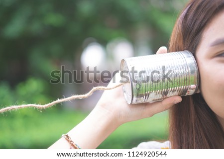 a girl listening through the tin can telephone, communication concept like a Telegram. The old days toy. Royalty-Free Stock Photo #1124920544
