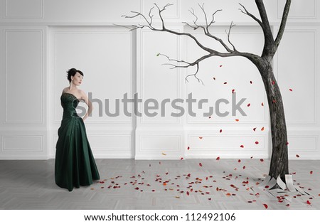 Old tree with falling leaves in a white room. Beautiful girl in front of the tree. A symbol of the fall.