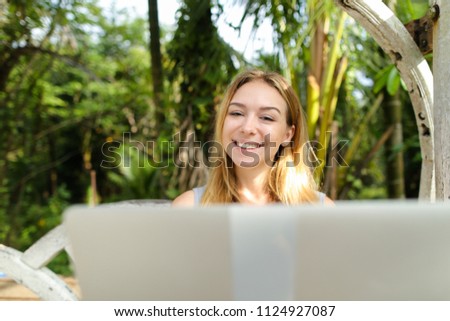 Young happy woman using laptop, palms in background. Concept of exotic resort and modern technology.