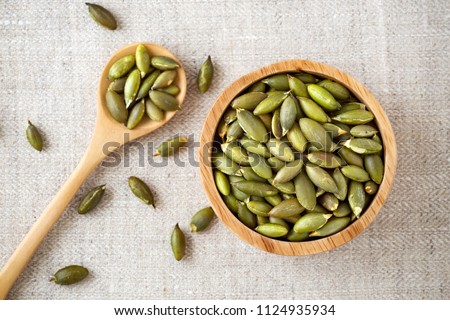 Pumpkin seeds in wooden bowl and spoon, top view