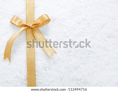 Decorative simple gold ribbon and bow on a background of winter snow with copyspace for your Christmas or festive greeting