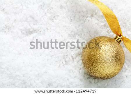 Shiny gold glitter bauble with a twirled golden ribbon on winter snow with copyspace for your Christmas message