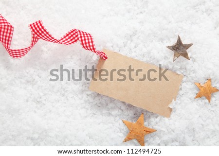 Blank Christmas gift label with a decorative red and white checked rustic ribbon surrounded by stars on fresh winter snow
