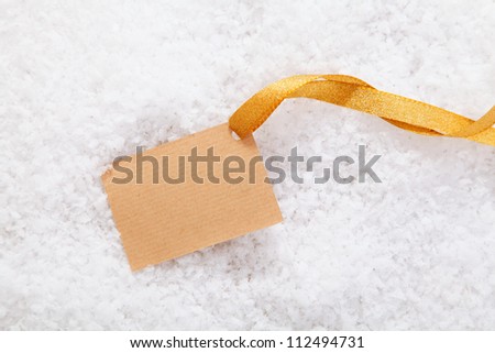 Empty blank paper label and gold ribbon lying in winter snow ready for your Christmas greeting