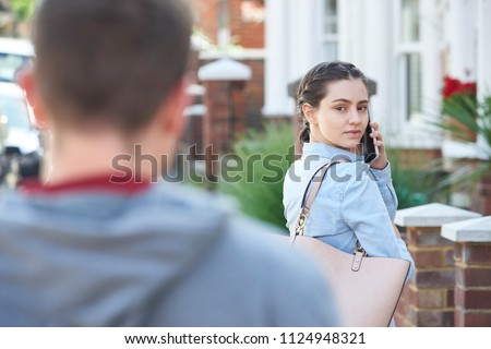 Young Woman Calling For Help On Mobile Phone Whilst Being Stalked On City Street By Man Royalty-Free Stock Photo #1124948321