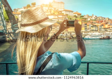 Happy blonde woman - tourist shot on her smartphone camera beautiful city view with ships on the river in sunny day.