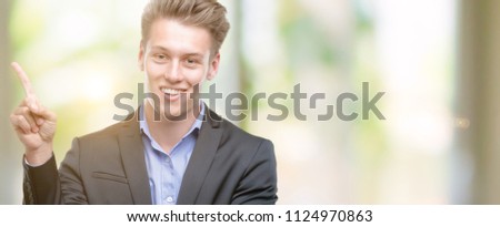 Young handsome blond business man very happy pointing with hand and finger to the side