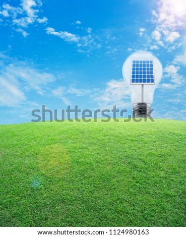 Light bulb with solar cell inside and green grass field over blue sky, Energy conservation and environmental concept