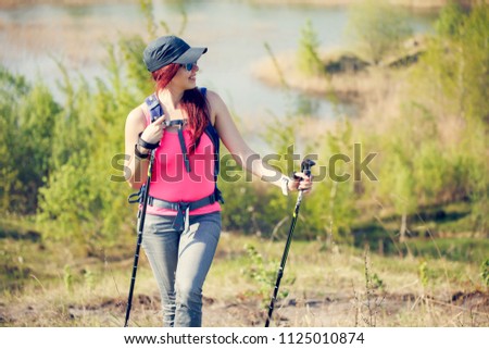 Image of young sporty girl looking away with walking sticks on background of lake and green vegetation