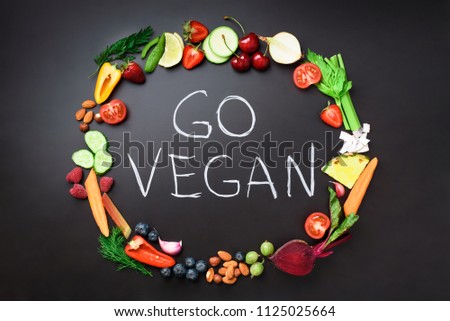 Healthy food background. Circle of fresh vegetables, fruits, nuts, berries with handwritten phrase Go Vegan on black chalkboard. Top view. Vegetarian, vegan, detox and clean eating concept.