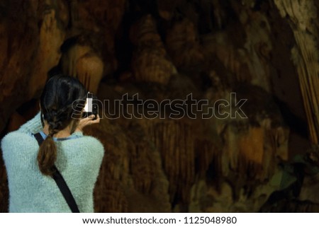 young woman take photo of stone cave. tourist take picture of cavern with stalactite.