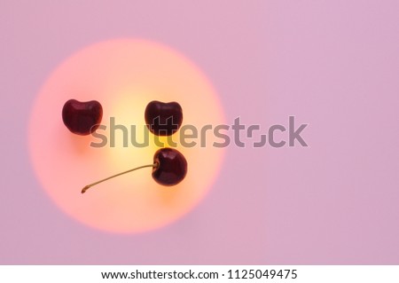 Red cherry fruits put on the orange color circle set as boring emoji emotion face with pink background that have space for text.