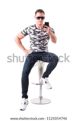 Handsome guy with sunglasses sitting on bar stool taking photo with smart phone. Full body isolated on white background.