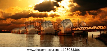 Thames Barrier, tidal protector, over dramatic sunset, commissioned by the Greater London Council, was complete by 1982, the world's second largest movable flood barrier. Royalty-Free Stock Photo #1125083306