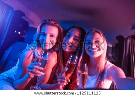 Beautiful and pretty girls are looking on camera and taking picture. They are holding glasses of champagne and smiling. Girls are posing on camera.