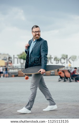 handsome bearded man with longboard walking in city
