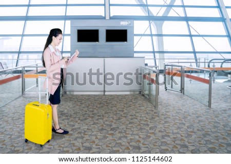 Picture of Caucasian businesswoman using a digital tablet while standing with a luggage in the airport terminal