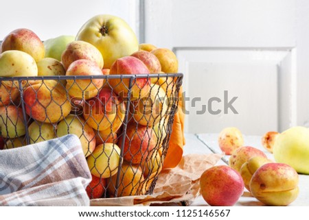 Ripe tasty fresh apricots and apples in  woven metal basket on wooden table in the room