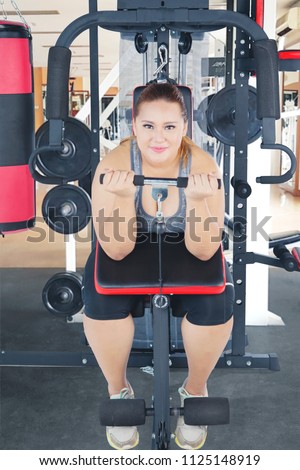 Picture of overweight woman smiling at the camera while using a gym machine. Shot in the gym center