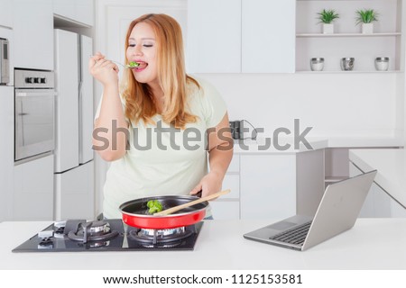 Picture of beautiful fat woman tasting food while standing in the kitchen