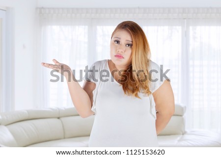 Picture of young fat woman looks confused while standing in the living room