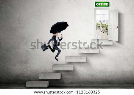 Picture of Asian businesswoman carrying a suitcase and umbrella while running on the stair toward the office door