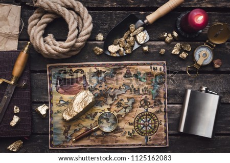 Old treasure map on adventurer or pirate table. Gold nuggets in shovel, compass, dagger, magnifying glass, rope and diary book on explorer desk.