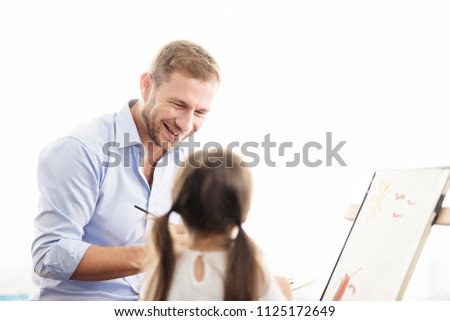 Young father teaching daughter to draw a picture. Happy time together. Setup studio shooting. Selective focus at father.