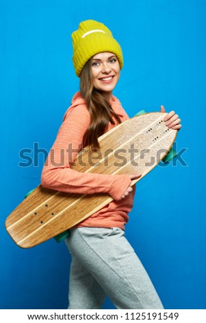 Healthy and beauty girl holding skateboard. Portrait on blue wall back.