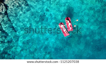 Aerial drone bird's eye top view of couple sitting in inflatable matress in rocky emerlad water tropical caribbean resort
