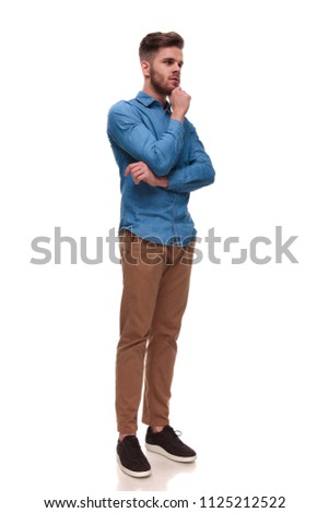 pensive casual man with beard looks to side while standing on white background, full body picture