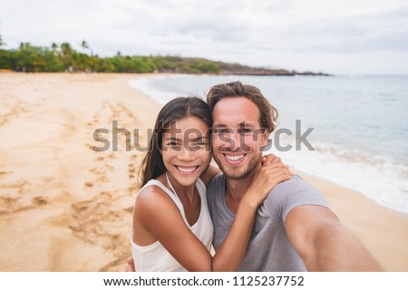 Two friends taking self portrait picture with phone. Smiling young interracial couple taking selfie on vacation travel. Asian woman, Caucasian man. Two young adults happy.