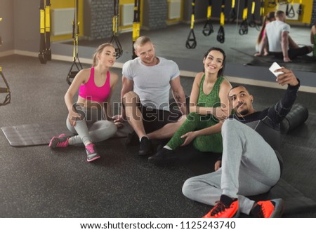Young multiethnic group making selfie at gym. Athlete men and women taking photo on smartphone having break after training, copy space