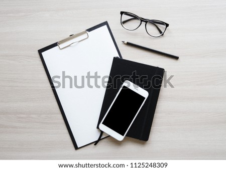 Flat lay stylish mockup photo with phone, blank paper, pencil, eye glasses and black notebook on the light wooden table background. Stock photo for blog and website.