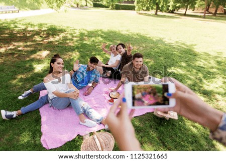 friendship, leisure and technology concept - group of happy smiling friends with non alcoholic drinks taking picture by smartphone on picnic at summer park