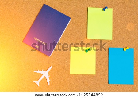 White model of passenger plane with blue passport and blue, orange, yellow paper note pin on cork board. Blank notes for add text message or design website. sticker note, copy space.
