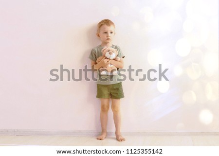 Sad child with a toy in his hands on the background of the wall flooded with sunlight. Copy space