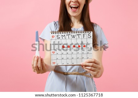 Cropped happy woman in blue dress, hat hold in hand pregnancy test, periods calendar for checking menstruation days isolated on pink background. Medical, healthcare, gynecological concept. Copy space Royalty-Free Stock Photo #1125367718