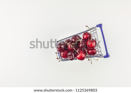 Creative top view of ripe cherries in a shopping cart with copy space isolated on white background in minimal style. Concept of supermarket or fruit market shopping. Template for your text or design.