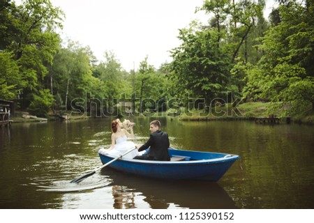 Wedding couple in the boat. The bride and groom are swimming in a boat on the lake. Wedding in the forest.  
Wedding couple on the lake. Blue boat, river