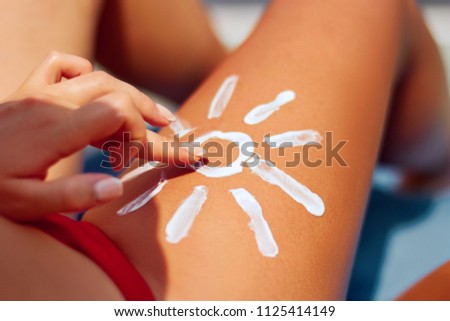 Sunbath protection. Woman using Suntan Lotion At The Beach In Form Of The Sun on leg