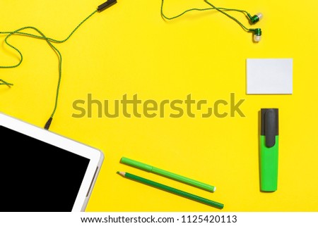 set of business gadgets and accessories from the top view. green pencils, headphones, paper stickers, markers and tablet pc lying on a yellow background. free space for text
