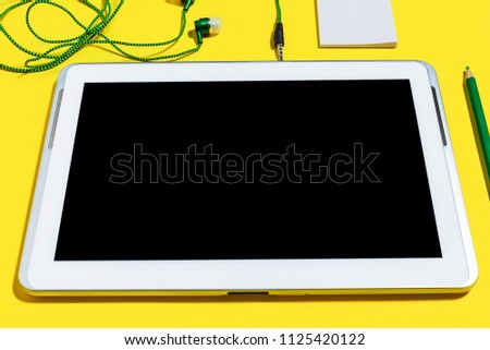 set of business or education accessories. green pencils, headphones, paper stickers, markers and tablet pc lying on a yellow surface. concept of the office gadgets