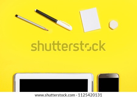 felt pen, pencil, rubber and paper stickers lying in front of smartphone and tablet pc at the yellow background. concept of office or educational chancery and gadgets. free copyspace. top view