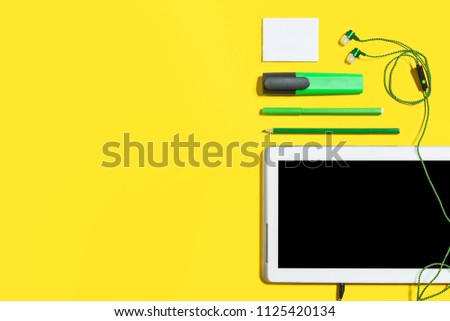 set of business or education accessories. green pencils, headphones, paper stickers, markers and tablet pc lying on a yellow surface. concept of the office chancery and gadgets. free copyspace