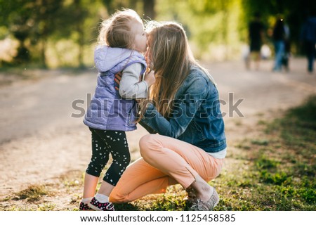 Happy smiling mother hugging her lovely little daughter outdoor. Lifestyle family. Adult cheerful female parent playing with her beautiful emotional child at nature in summer. Positive people faces