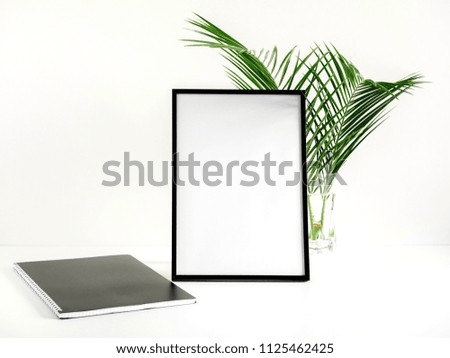 Front view blank mock up of photo frame on white background, notebook,  green plant. Flat lay, top view, copy space