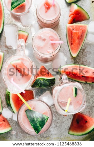 Watermelon an strawberry agua fresca cocktail , summer fresh drink on different glass container over a silver plate background and with pics of watermelon and melted ice around
