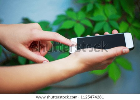 Woman holding smartphone outdoors near the wall and plant on it.